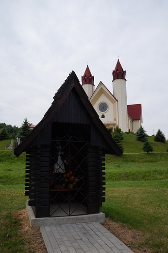 Szlak Jana Nepomucena - drewniana kapliczka z Janem na tle Sanktuarium MB Pocieszenia